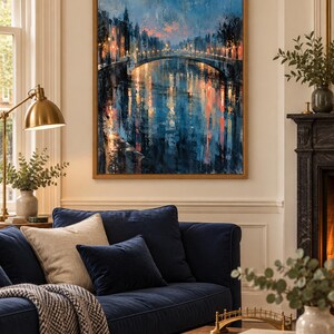 May include: A framed vertical wall art print depicting a city canal scene at twilight. The painting features a stone bridge illuminated by warm streetlights, with deep blue and orange reflections shimmering on the water surface in a textured style.