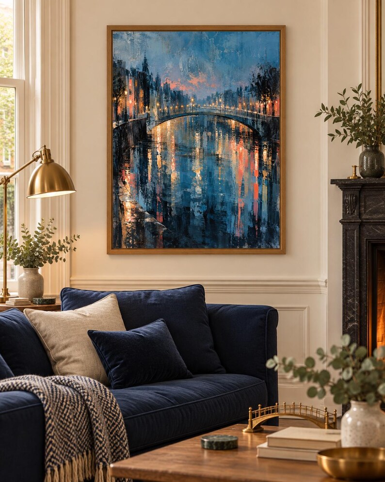 May include: A framed vertical wall art print depicting a city canal scene at twilight. The painting features a stone bridge illuminated by warm streetlights, with deep blue and orange reflections shimmering on the water surface in a textured style.