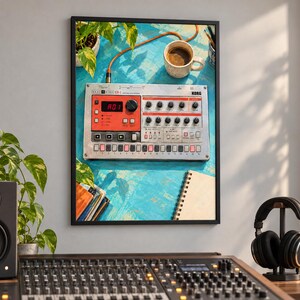 Puede incluir: Una impresi&oacute;n de arte de pared enmarcada que muestra una caja de ritmos Korg Electribe ER-1 plateada sobre una superficie azul texturizada. La imagen incluye una taza de caf&eacute; blanca, un cuaderno de espiral y hojas de plantas verdes alrededor.
