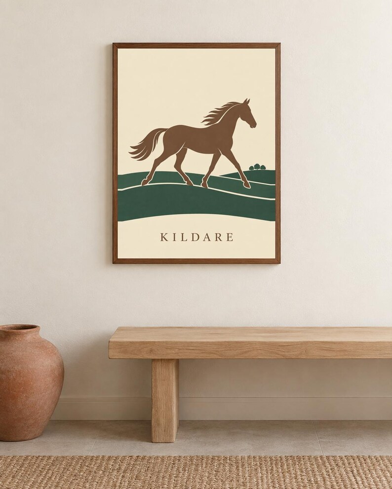 May include: A framed wall art print featuring a brown horse galloping across green rolling hills against a cream background. The word KILDARE is printed in dark brown capital letters at the bottom center of the rectangular print.
