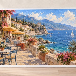 May include: A framed landscape painting depicting a coastal Mediterranean scene with an outdoor cafe terrace, blue chairs, yellow umbrellas, and potted pink flowers overlooking a deep blue sea with sailboats under a bright, cloud-filled sky.