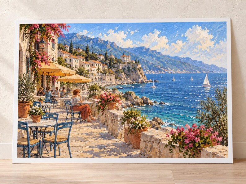 May include: A framed landscape painting depicting a coastal Mediterranean scene with an outdoor cafe terrace, blue chairs, yellow umbrellas, and potted pink flowers overlooking a deep blue sea with sailboats under a bright, cloud-filled sky.