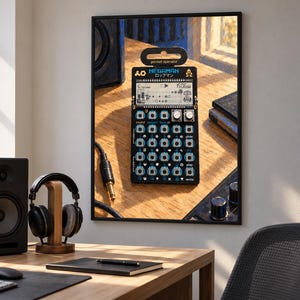 May include: A black Teenage Engineering Pocket Operator synthesizer featuring a Megaman graphic, a digital LCD screen, multiple circular buttons, and two silver knobs. The device is displayed in a black frame, showcasing its compact design.