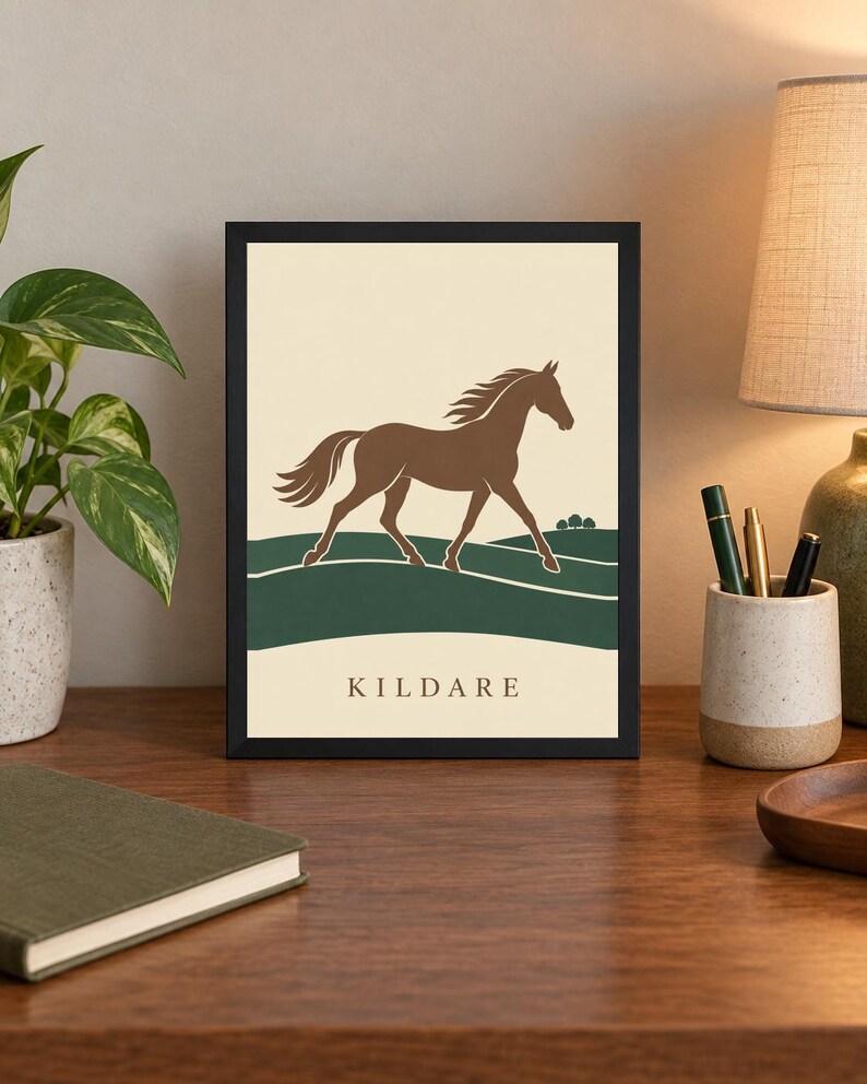 May include: A framed rectangular print featuring a brown horse silhouette galloping across a dark green landscape against a cream background. The word KILDARE is printed in a simple serif font at the bottom center of the artwork within the frame.