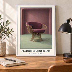 May include: A framed art print featuring a Platner lounge chair with a deep purple upholstered seat and a gold-toned wire base. The chair is set against a mauve arched wall and a light green floor. The text reads PLATNER LOUNGE CHAIR Warren Platner.