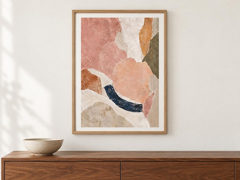 May include: A framed rectangular wall art print featuring an abstract composition of layered organic shapes in shades of dusty pink, terracotta, cream, olive green, and a deep navy blue curved brushstroke, all enclosed in a light wood frame.