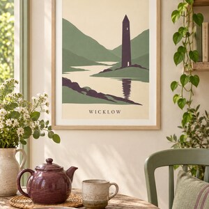 Peut inclure: Une affiche murale encadr&eacute;e repr&eacute;sentant une illustration de paysage stylis&eacute;e avec une haute tour sombre situ&eacute;e pr&egrave;s d'une rivi&egrave;re et des collines vertes en arri&egrave;re-plan. L'impression inclut le texte WICKLOW centr&eacute; en bas en police serif.