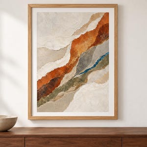 May include: A framed wall art print featuring an abstract composition of layered, torn-paper style shapes in shades of burnt orange, olive green, slate gray, and cream, set within a light-toned wooden frame with a clean, rectangular border.