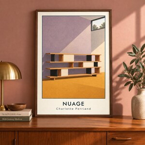 May include: A framed art print titled NUAGE by Charlotte Perriand, featuring a stylized illustration of a wooden shelving unit with black and white accents against a purple wall and yellow floor, set within a dark wood frame on a wooden surface.