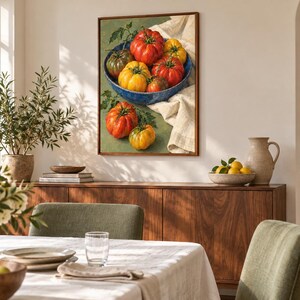 May include: A framed wall art print depicting a still life of heirloom tomatoes in a blue bowl. The composition features red, yellow, and green tomatoes with green stems, resting on a white cloth against a muted green background.