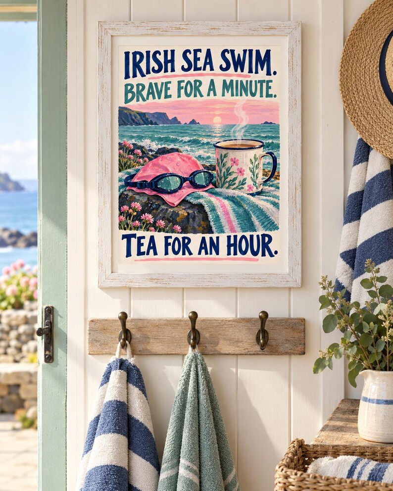 May include: A framed wall art print featuring a coastal scene with a pink swim cap, goggles, and a floral mug. The text reads: IRISH SEA SWIM. BRAVE FOR A MINUTE. TEA FOR AN HOUR. The illustration includes a sunset over the ocean and rocky cliffs.