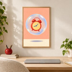 May include: A framed wall art print featuring a red analog alarm clock with a yellow face and blue hands, encased inside a translucent, iridescent bubble against a solid peach-colored background, positioned above a light beige surface.