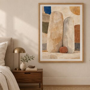 May include: A framed wall art print featuring an abstract composition of two large, upright, textured stone-like shapes in beige and light gray, accented by a small terracotta-colored sphere, set against a background of layered, muted color blocks.