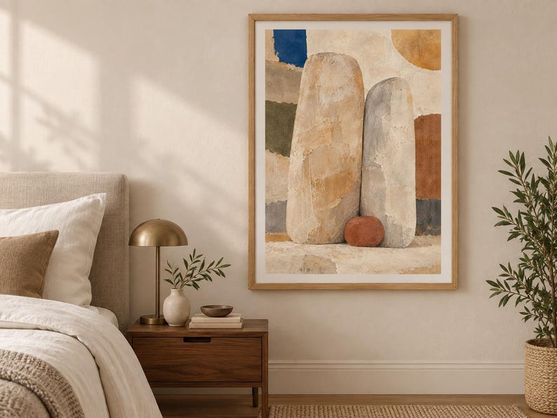 May include: A framed wall art print featuring an abstract composition of two large, upright, textured stone-like shapes in beige and light gray, accented by a small terracotta-colored sphere, set against a background of layered, muted color blocks.