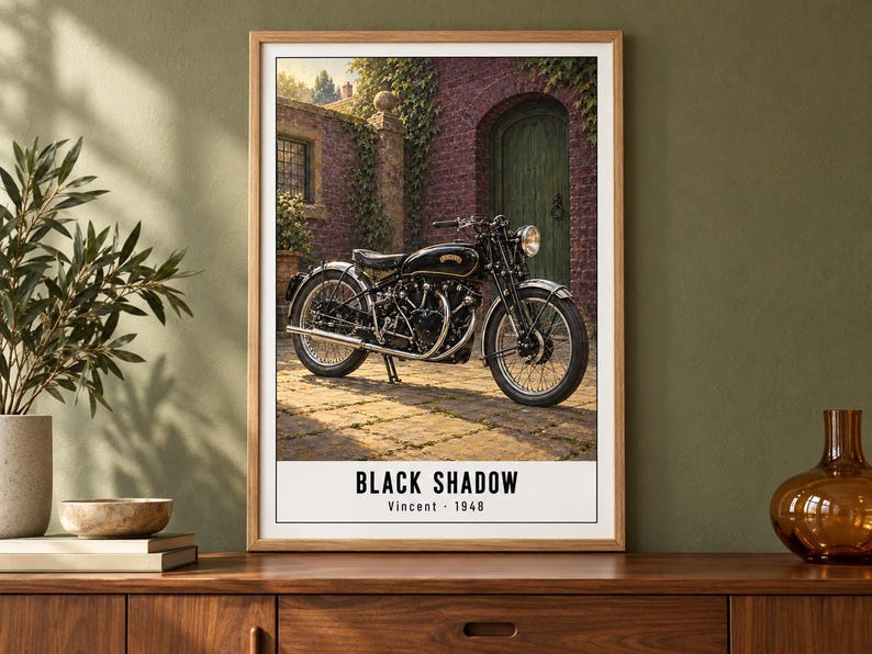 Peut inclure: Une affiche encadr&eacute;e repr&eacute;sentant une moto noire vintage gar&eacute;e sur une terrasse en pierre devant un b&acirc;timent en briques avec une porte verte. Le texte en bas indique BLACK SHADOW Vincent - 1948 dans une police noire sans empattement.