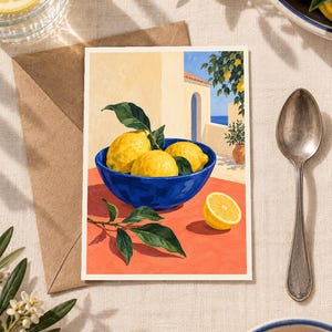 May include: A rectangular art print featuring a painting of three bright yellow lemons in a deep blue bowl, placed on a vibrant orange surface. The background depicts a sunlit Mediterranean-style building with an archway, blue sea, and lemon tree.