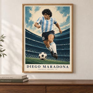 K&ouml;nnte beinhalten: Ein gerahmtes Poster mit einem Fu&szlig;ballspieler in einem hellblau-wei&szlig; gestreiften Trikot und schwarzen Shorts, der einen Fu&szlig;ball auf einem Spielfeld tritt. Der Hintergrund zeigt ein Stadion mit hellem Himmel. Der Text lautet DIEGO MARADONA FOOTBALL LEGENDS 07.