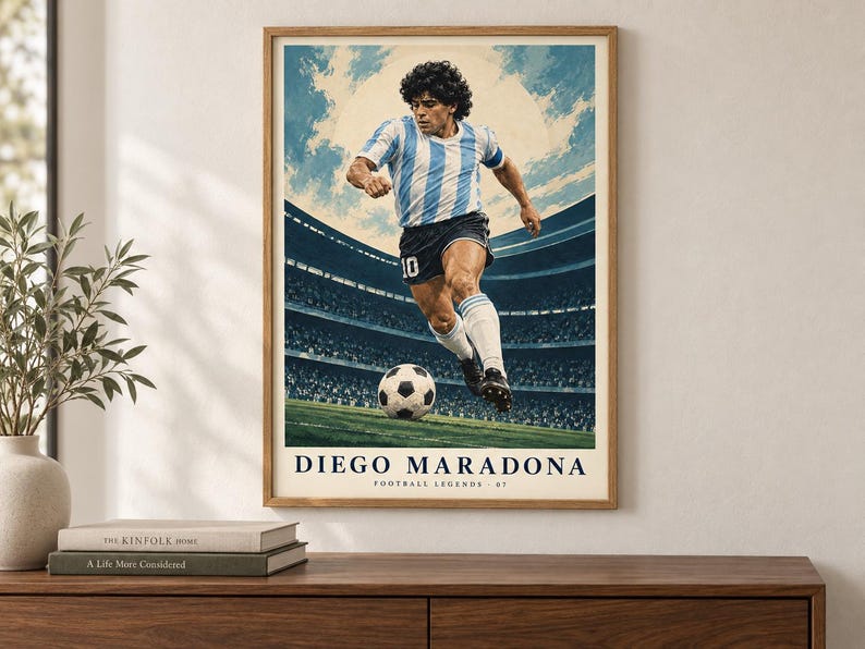 K&ouml;nnte beinhalten: Ein gerahmtes Poster mit einem Fu&szlig;ballspieler in einem hellblau-wei&szlig; gestreiften Trikot und schwarzen Shorts, der einen Fu&szlig;ball auf einem Spielfeld tritt. Der Hintergrund zeigt ein Stadion mit hellem Himmel. Der Text lautet DIEGO MARADONA FOOTBALL LEGENDS 07.
