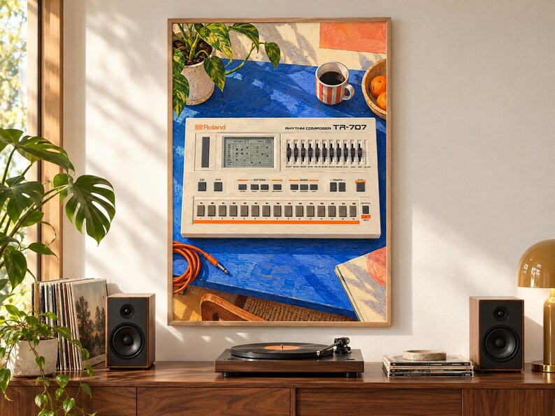 May include: A framed art print depicting a vintage Roland TR-707 Rhythm Composer drum machine on a bright blue table. The scene includes a potted plant, a striped mug, and oranges. The drum machine features a digital display, sliders, and buttons.