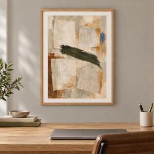 May include: A framed abstract wall art print featuring layered rectangular shapes in shades of beige, cream, and brown, accented by a bold, horizontal dark green brushstroke across the centre and a small patch of bright blue in the upper corner.