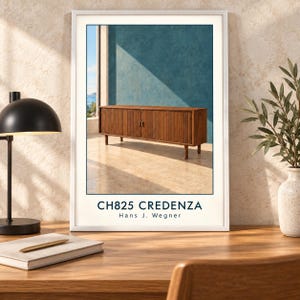 May include: A framed art print featuring a brown wooden credenza with vertical slatted doors and thin legs. The text on the print reads CH825 CREDENZA Hans J. Wegner. The credenza is set against a blue wall with sunlight casting shadows.