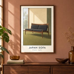 Pu&ograve; includere: Una stampa artistica da parete incorniciata che raffigura un divano in legno con cuscini grigio scuro, posizionato contro una parete chiara e un pavimento verde. Il testo JAPAN SOFA e Finn Juhl &egrave; stampato in nero sul bordo bianco del poster.