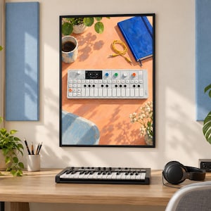 Pu&ograve; includere: Una stampa da parete incorniciata che mostra una vista dall'alto di un sintetizzatore portatile bianco con tastiera, manopole colorate e un piccolo schermo, posizionato su una superficie arancione accanto a un taccuino blu, un cavo giallo e una tazza di caff&egrave;.