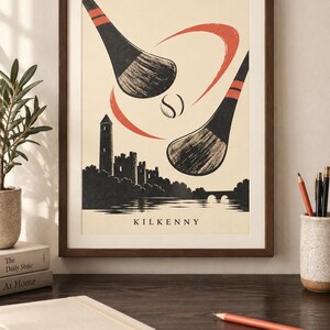 Peut inclure: Une impression d'art encadr&eacute;e illustrant deux crosses de hurling et une balle au-dessus de la silhouette du ch&acirc;teau de Kilkenny et d'une rivi&egrave;re. L'affiche est cr&egrave;me avec des d&eacute;tails noirs et rouges et le mot KILKENNY inscrit en bas.