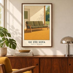 May include: A framed wall art print featuring a mid-century modern style sofa with olive green cushions and a light wood frame. The illustration depicts the GE 290 SOFA by Hans J. Wegner set against a warm yellow floor and a sunlit interior.