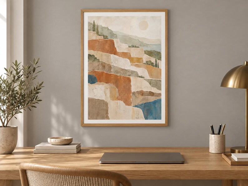 Op de afbeelding: Een ingelijste verticale wandkunstprint met een gelaagde landschapsillustratie, een bleke zon, terrasvormige heuvels in tinten terracotta, beige en saliegroen, en diepblauwe wateraccenten, gevat in een lichthouten lijst.