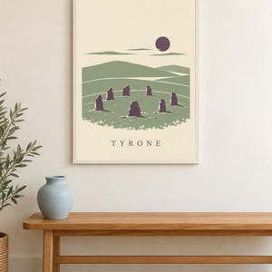 May include: A rectangular wall art print in a light frame featuring a graphic illustration of a stone circle in a green landscape under a dark purple sun. The word TYRONE is printed in capital letters at the bottom of the cream-colored background.