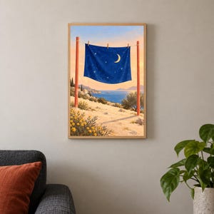 May include: A framed wall art print depicting a dark blue fabric sheet with a crescent moon and star pattern hanging on a clothesline between two red wooden posts. The scene features a coastal landscape with yellow flowers and a calm sea.