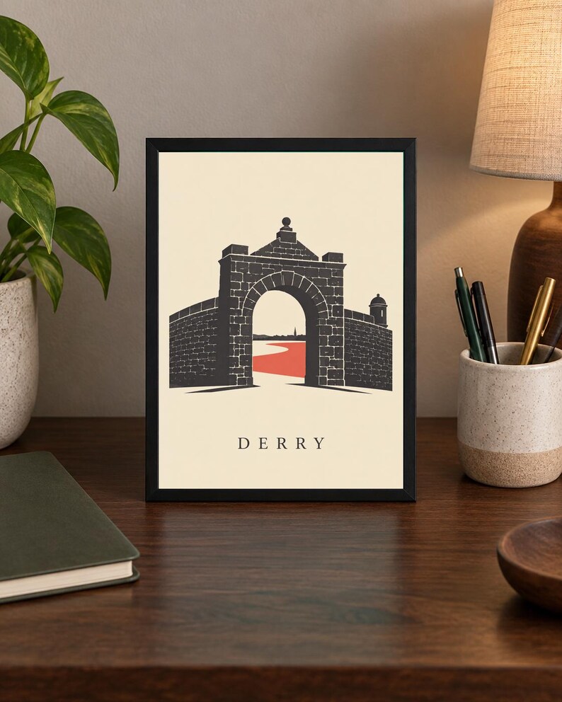 May include: A framed art print featuring a black graphic illustration of the historic stone city walls and arched gate of Derry. The design includes a red path leading through the archway against a cream background with the text DERRY below.