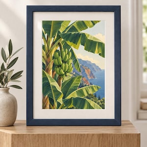 May include: A framed art print featuring a vibrant illustration of a banana tree with a large bunch of green bananas hanging from the stalk. The background depicts a coastal landscape with blue ocean waters, rocky cliffs, and a clear sky.