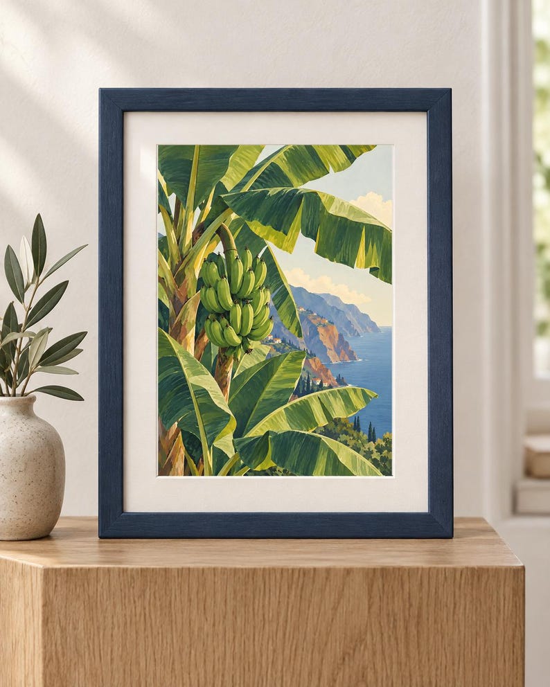 May include: A framed art print featuring a vibrant illustration of a banana tree with a large bunch of green bananas hanging from the stalk. The background depicts a coastal landscape with blue ocean waters, rocky cliffs, and a clear sky.