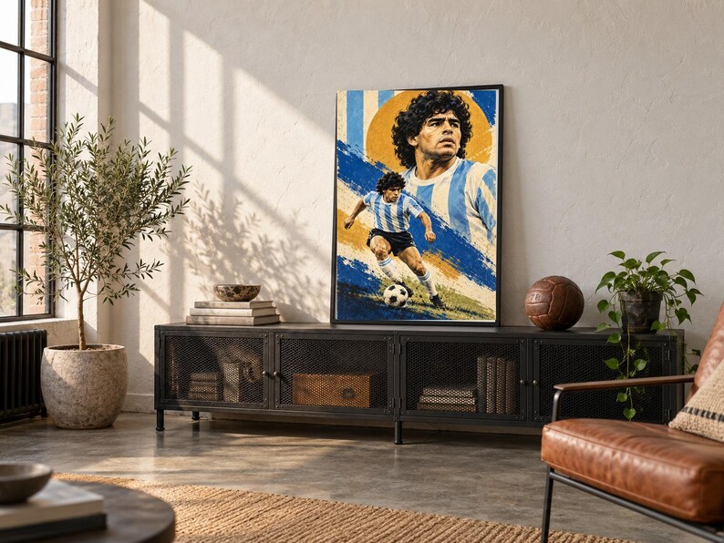 May include: A framed vertical poster featuring a stylized illustration of Diego Maradona in a light blue and white striped soccer jersey. The artwork displays a large portrait above a smaller action shot of the player running with a soccer ball.