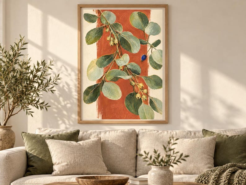 May include: A framed wall art print featuring a botanical illustration of a leafy branch with green foliage, small pale yellow berries, and a single blue berry, set against a vertical terracotta orange brushstroke on a cream background.