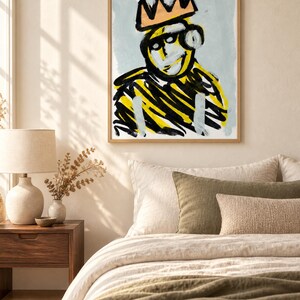 May include: A framed wall art print featuring an abstract figure wearing a crown. The figure is rendered in bold black and yellow brushstrokes against a light blue background. The crown is painted in a muted orange tone, and the artwork is enclosed in a simple light-colored wooden frame.