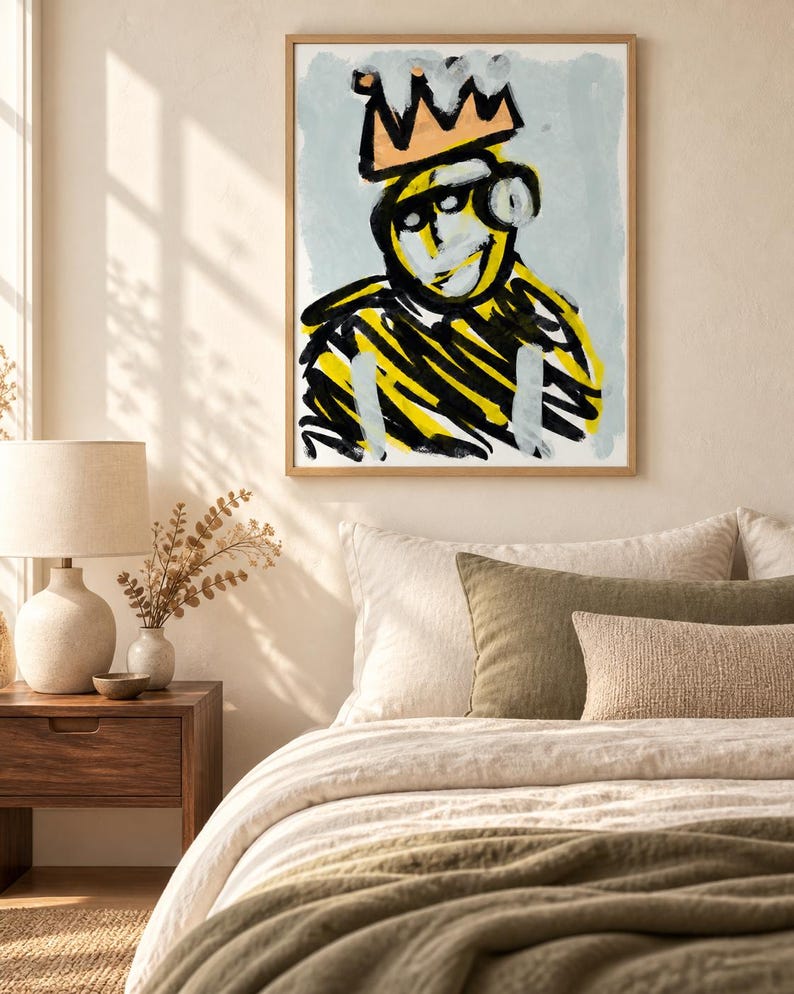 May include: A framed wall art print featuring an abstract figure wearing a crown. The figure is rendered in bold black and yellow brushstrokes against a light blue background. The crown is painted in a muted orange tone, and the artwork is enclosed in a simple light-colored wooden frame.