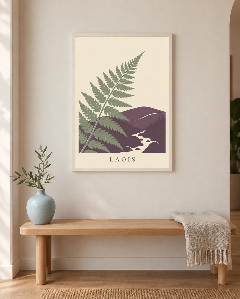 May include: A rectangular wall art print in a light-coloured frame featuring a stylised green fern frond overlapping a dark purple landscape with a winding white river and hills. The word LAOIS is printed in black capital letters at the bottom.
