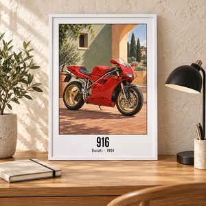 May include: A framed wall art print featuring a red Ducati 916 motorcycle parked on a terracotta patio. The image shows the bike in profile with gold wheels. Below the illustration, the text reads 916 and Ducati 1994 in black font.