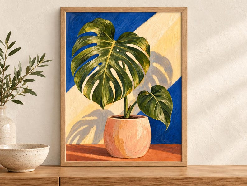 Puede incluir: Un cuadro enmarcado de una planta monstera en una maceta color melocot&oacute;n claro. La planta tiene hojas verdes grandes y divididas. El fondo presenta una divisi&oacute;n diagonal en azul oscuro y amarillo p&aacute;lido, con una sombra proyectada en la zona amarilla.