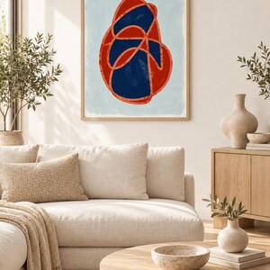 May include: A framed wall art print featuring a central abstract shape composed of a dark navy blue organic form outlined by a thick, textured orange line, set against a light blue background within a light-toned wooden frame.