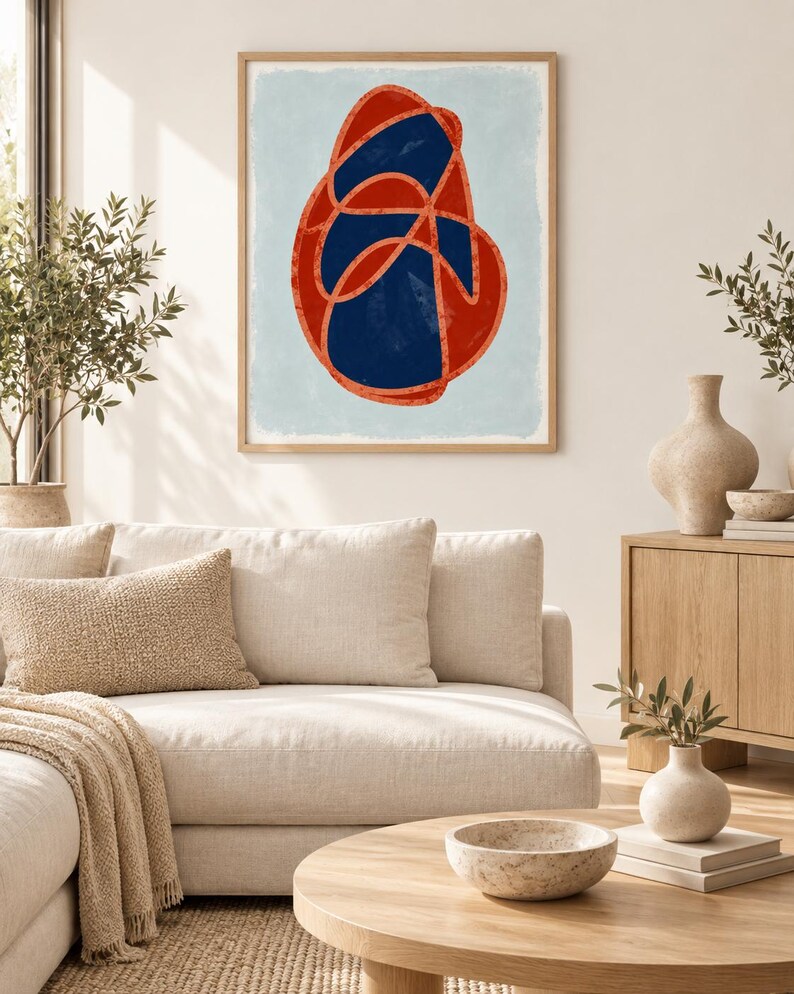 May include: A framed wall art print featuring a central abstract shape composed of a dark navy blue organic form outlined by a thick, textured orange line, set against a light blue background within a light-toned wooden frame.