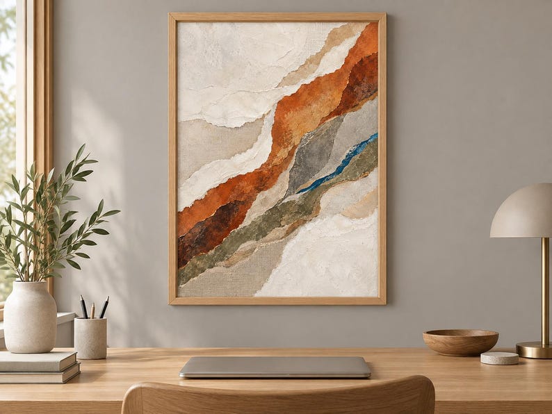 May include: A framed abstract wall art piece featuring layered, torn-paper style textures in earthy tones of cream, beige, burnt orange, deep brown, olive green, and a thin streak of vibrant blue, all enclosed within a light-colored wooden frame.
