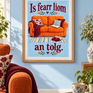 K&ouml;nnte beinhalten: Ein gerahmter Kunstdruck mit einer Illustration eines leuchtend orangefarbenen Sofas auf hellblauem Grund. Der Text "Is fearr liom an tolg" ist in dunkelroten Buchstaben geschrieben. Das Sofa hat eine weinrote Decke, Kissen und Hausschuhe.