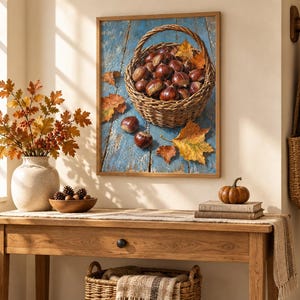 May include: A framed wall art print featuring a woven basket filled with brown chestnuts resting on a weathered blue wooden surface, accented by scattered autumn leaves. The artwork displays a rustic harvest theme with warm orange and brown tones.