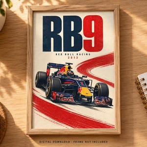 May include: A framed poster featuring a dark blue and red Formula One race car on a track. The text RB9, RED BULL RACING, and 2013 are printed above the car. A red brushstroke graphic curves across the background. The bottom text reads DIGITAL DOWNLOAD.