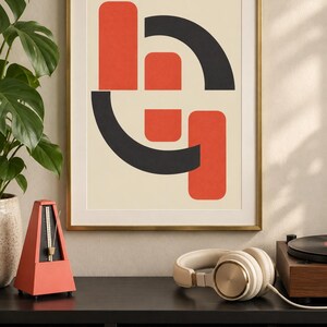 May include: A framed wall art print featuring a geometric composition of two vertical orange rectangles and two black curved arcs on a cream background. The artwork is enclosed in a thin gold-colored metal frame, displaying a balanced arrangement of shapes.