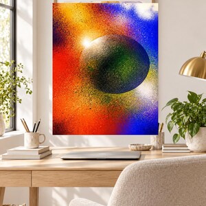 Op de afbeelding: Een rechthoekige wandkunstprint met een centrale donkere bol omringd door een levendig spuitverf-neveleffect. De achtergrond toont een verloop van fel oranje, geel en diepblauwe kleuren met een gespikkeld en getextureerd uiterlijk.